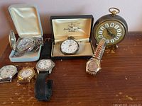 Photo of the lot showing multiple wristwatches including a vintage pocket watch in Weber box and a brass desk clock