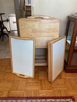 Wooden folding TV tables, two trays, and stand arranged on a wood floor near furniture and kitchen area.