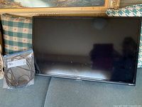 Front view of TCL Roku TV on fabric surface alongside remote control in plastic bag