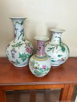 Three porcelain vases displayed together on wooden furniture with floral and bird designs.
