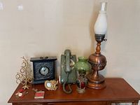 Wide shot of all items including vintage wall phone, decorative lamps, black mantel clock, and small decorative pieces arranged on table.