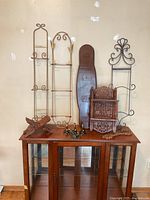 Full view of all wall decor and display items arranged on and above a glass-front wooden cabinet, showing two metal racks, wooden paddle, wooden shelf, metal hooks, and stands.