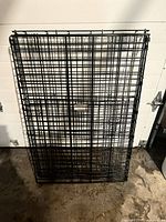 Folded black wire dog crate leaning on garage wall