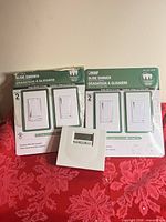 Front view showing two packaged Feit Electric slide dimmers and unboxed white digital thermostat