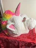 Side view of plush unicorn head showing rainbow mane, horn, ears