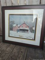 Framed serigraph showing a winter landscape with a pink house and snow