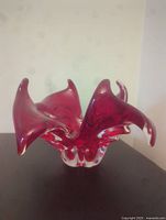 Front view of red crystal ornate bowl with curved flowing edges on dark surface.