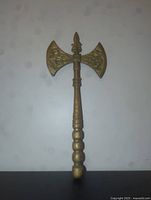 Front view of the brass double-headed ax showing full length, rounded segmented handle, and elaborate winged sculptures on blade edges.