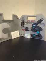 Full microscope set displayed open in hard plastic carry case, showing microscope, slides, tools, and accessories.