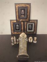 Photo showing entire lot including the bronze/brass sarcophagus figurine at center, six smaller Egyptian god and pharaoh figurines around it, and three framed Egyptian mask artworks behind them.