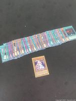 Image showing a spread of approximately 90 Yu-Gi-Oh cards laid out in a row with one card placed separately in front.