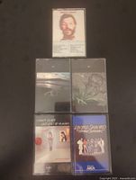 Five vintage cassette tapes placed on a dark surface, showing front covers including Ringo Starr, two Led Zeppelin tapes, Robert Plant, and Lynyrd Skynyrd.