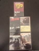 Front view of five vintage cassette tapes in their cases laid out for display showing album covers: The Doors L.A. Woman, Skid Row, War of the Worlds, U2 Joshua Tree, and ZZ Top Best of ZZ Top.