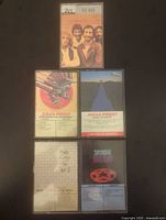 Front view of the five cassette cases showing album art images for The Who, Judas Priest (two albums), Rush, and Pink Floyd.