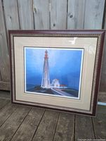 Framed limited edition print of Lawren Harris's Lighthouse Father Point placed on wooden floor outdoors showing entire frame and artwork.