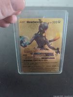 Front view of 2020 Mewtwo GX gold foil Pokémon card in top loader case showing character, HP, moves, and details in black text on a gold holographic background.