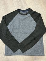 Full image of grey body sweater with dark raglan sleeves laid flat