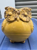 Front view of vintage mustard yellow ceramic owl figurine, showing large detailed eyes with brown accents and rounded body shape.