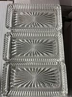 Top view of three rectangular crystal glass trays stacked to show starburst cut pattern and textured edges.