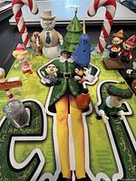 Top view of the Elf movie mini figure set on a backing card showing most figurines and props, including Buddy the Elf center, Santa, candy canes, and tree.