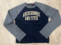 Front view of navy blue and grey raglan sleeve Abercrombie & Fitch muscle fit sweater with embroidered logo