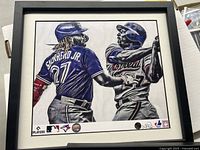 Framed print featuring Vladimir Guerrero Jr. and Sr. in action, showing back of Guerrero Jr. with number 27 jersey, artwork by Paul Jennis. Printed logos and signatures at bottom.