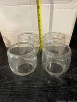 Four clear glass lantern globes arranged in a square pattern with a measuring tape indicating approximately 5 inches tall.