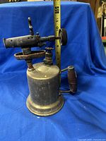 Side view of antique brass blow torch showing the cylindrical tank, wooden handle, and burner assembly with adjustment knob.