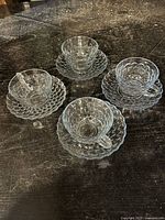 Four bubble glass tea cups each paired with a matching bubble glass saucer. Glass cups and saucers have a distinctive raised bubble texture and clear to slight blue tint.