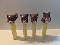 Photo showing four vintage MGM Pez dispensers with character heads Jerry, Spike, and two Tykes on yellow stems standing side by side against neutral background.