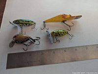 Four vintage Fred Arbogast fishing lures on white background next to ruler showing lengths from about 2 to 4 inches