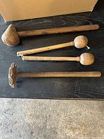 Four vintage wooden kitchen mallets arranged horizontally on a dark surface showing their different sizes and head shapes.
