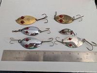 Photo showing six Hofschneider Red Eye Wiggler fishing lures of various sizes arranged with a ruler for scale on a white surface.