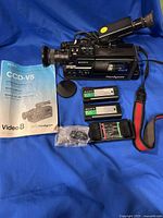 Sony Handycam CCD-V5 Video8 camera with batteries, battery charger, instruction manual, lens cover, carry strap, and accessory cable laid out on blue fabric.