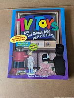 Front cover of the book showing the title, author, and colorful toy-figures imagery with light corner crease on bottom right.