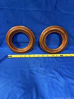 Two small round wooden frames placed on a blue fabric background with measuring tape showing approximately 6 inches diameter each.