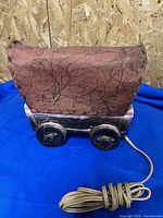 Photo of red fabric covered wagon TV lamp base with electrical cord extended on blue cloth background and wood wall backdrop