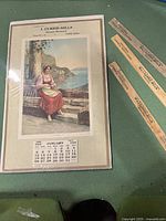 Photo showing the 1936 paper calendar with scenic painting and three wooden rulers with advertising branding