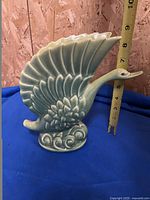 Side view of the swan vase on blue cloth background showing vase height with measuring tape approx 8 inches tall.