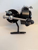 Side view of vintage black Mitchell 314 spinning reel with metal crank and black plastic grip, showing engraved details.