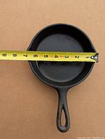 Top view showing the interior cooking surface and handle with a measuring tape showing approximately 7.5 inch diameter.