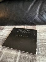 Black AC/DC Back in Black CD case closed and laying on a blanket.