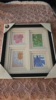 Photo of framed collage frame with four square photo openings, each containing a different floral image. Frame edge is black with white matting. Protective corner guards still on frame.