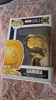 Front view of Gamora Funko Pop figure sealed inside a clear plastic window box with Marvel Studios and Pop branding, number 382. Box shows creased edges and wear.
