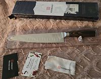 Keemake chef's knife with packaging and accessories on fabric background.