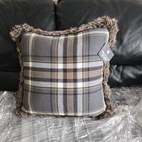 Front view of the square plaid flannel pillow with brown faux fur trim on a black leather couch, showing the pillow's overall look and color scheme.