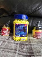 Front view of the sealed jar of yellow airsoft BBs with label visible, flanked by two smaller jars.