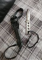 Photo showing diving knife with sheath and wrist strap on plaid fabric surface.