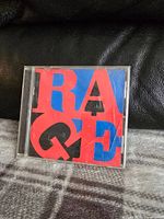 Front cover of the Rage Against The Machine CD album showing colorful letters RAGE on a red and blue background.