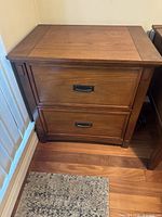 Front view of wooden two drawer lateral filing cabinet showing drawer fronts and metal handles.